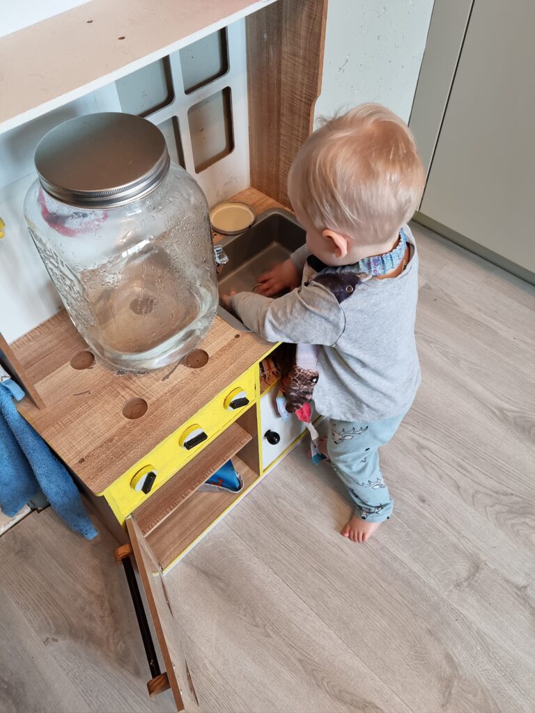 Väikelaps peseb mänguköögis käsi